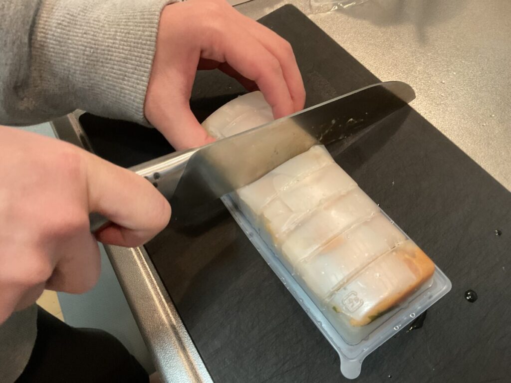 寿司が崩れないよう手で押さえながら、トレーの溝に合わせて切り分ける工程。